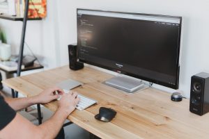 A person sitting at a keyboard and a desk with code on the screen, programmer coding devleoper